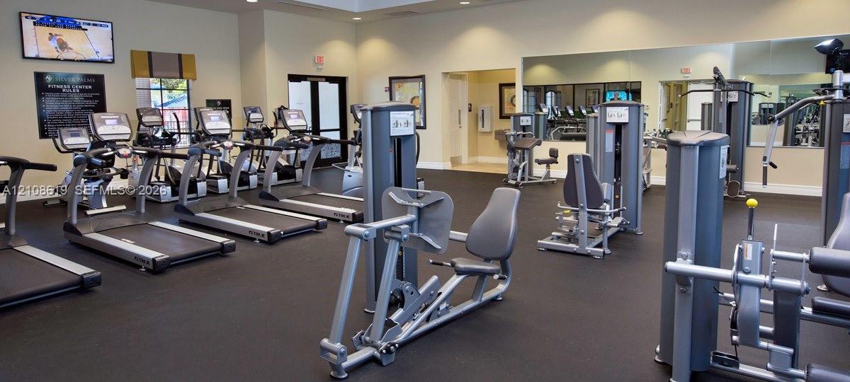 Fitness center featuring rubber flooring, wall-to-wall mirrors, and a selection of cardio and strength training equipment