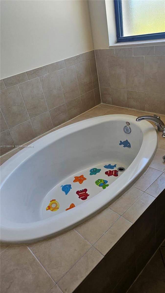 Oval soaking tub featuring neutral-toned tile surround, polished metal faucet, and privacy glass window