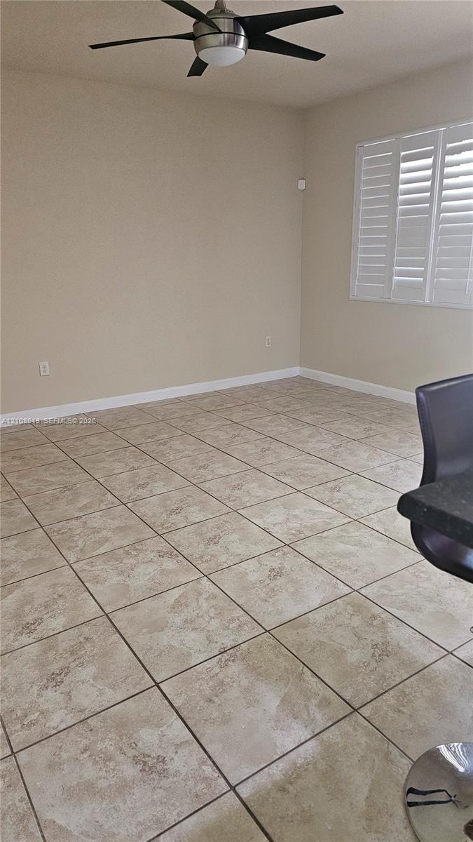 Interior space featuring large-format ceramic tile flooring, plantation shutters, and a multi-blade ceiling fan with integrated lighting