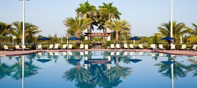 Swimming pool with surrounding paver deck, wooden pergola, and mature palm trees