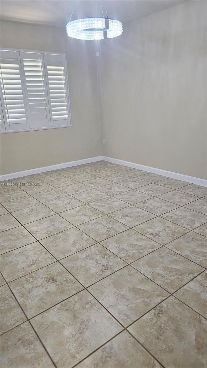 Neutral-toned tile flooring, circular tiered chandelier, and multi-panel window with plantation shutters