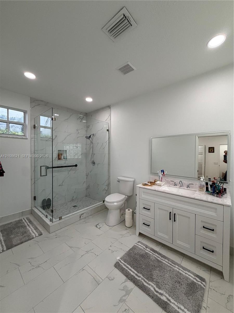 Bathroom featuring a glass-enclosed walk-in shower with tile surround, white vanity with stone countertop, recessed lighting, and large-format tile flooring