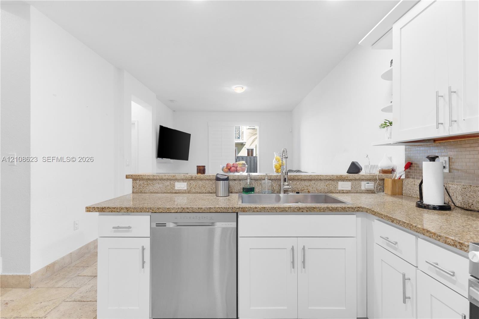 Kitchen featuring white cabinetry, stone countertops, stainless steel dishwasher, undermount sink with a gooseneck faucet, and tile flooring