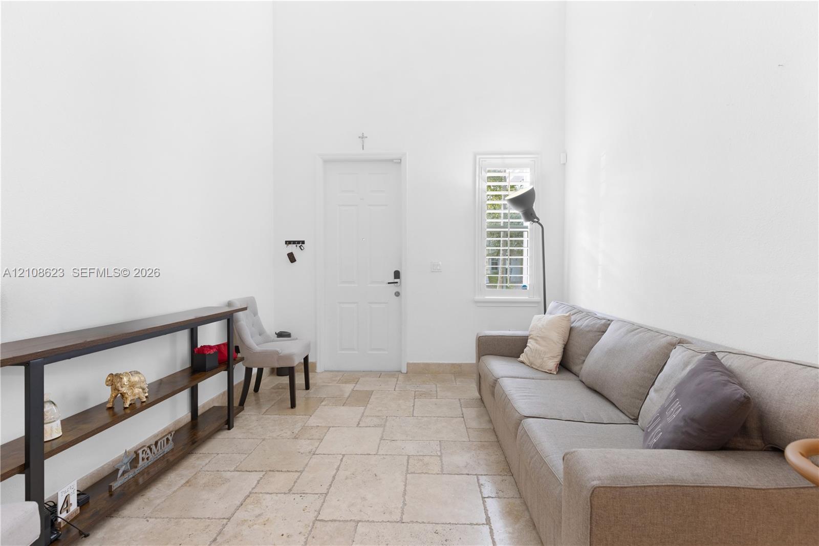 High-ceilinged entry featuring stone flooring, a multi-panel door, and a window with interior shutters