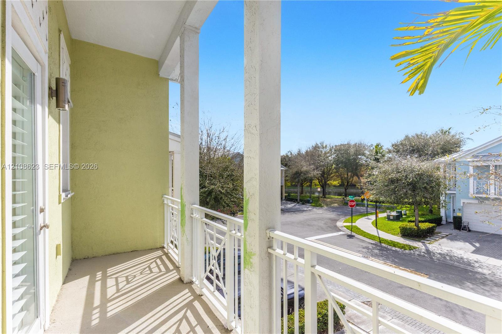 Covered balcony featuring white metal railings, structural support columns, and an exterior wall-mounted light fixture