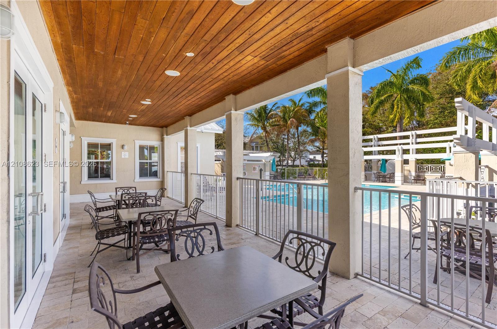 Covered patio featuring a wood-plank ceiling, natural stone flooring, and metal railings overlooking a swimming pool area