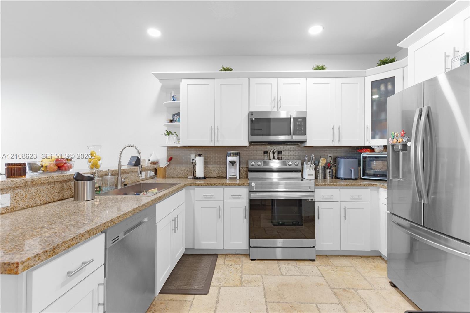 Kitchen featuring white shaker-style cabinetry, natural stone countertops, stainless steel appliances, and tile flooring