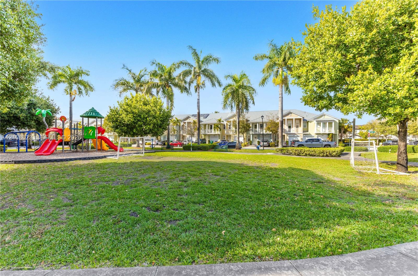 Common area featuring a manicured lawn, playground structure, mature palm trees, and perimeter landscaping