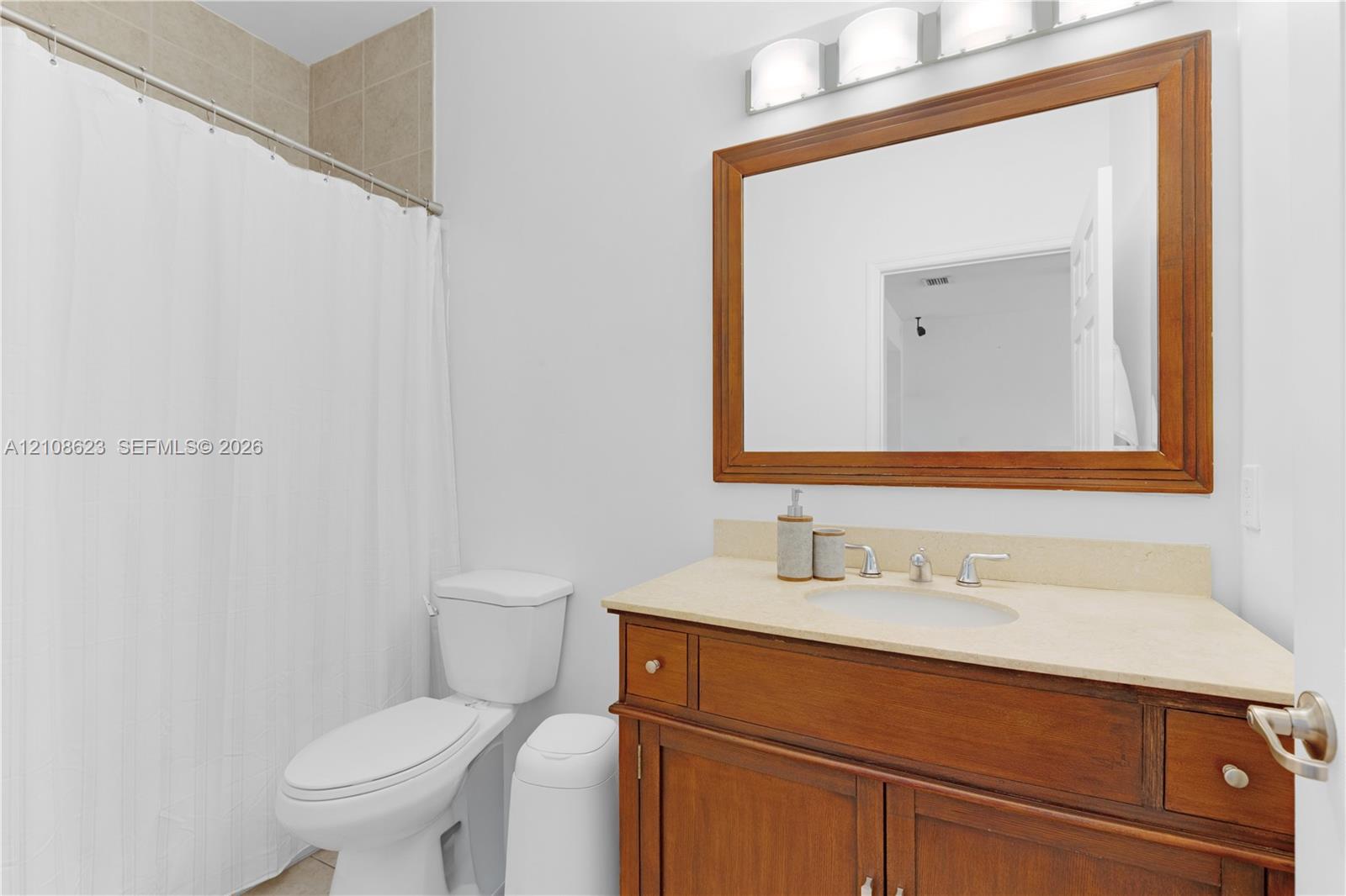 Bathroom featuring a wood-finish vanity with a neutral solid-surface countertop, an oval under-mount sink, a framed wall mirror, and a three-bulb vanity light fixture