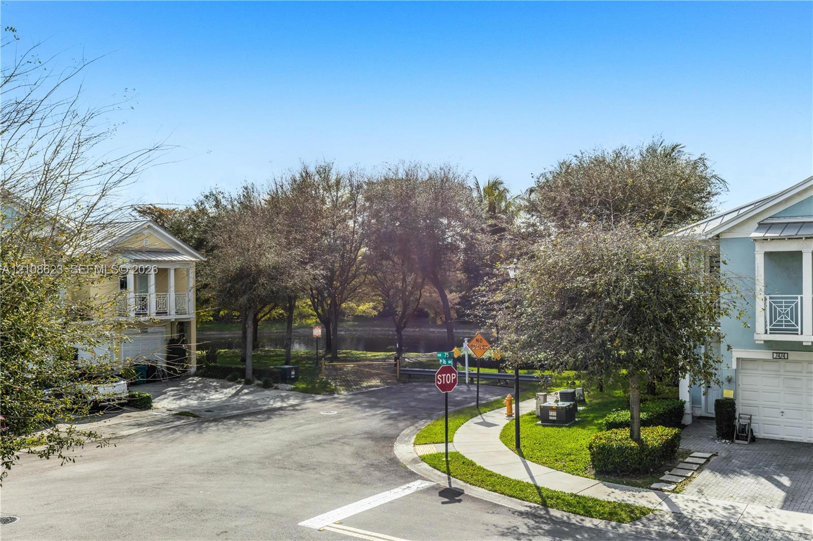 Exterior setting featuring paved street access, manicured lawn areas, mature tree canopy, and concrete sidewalk