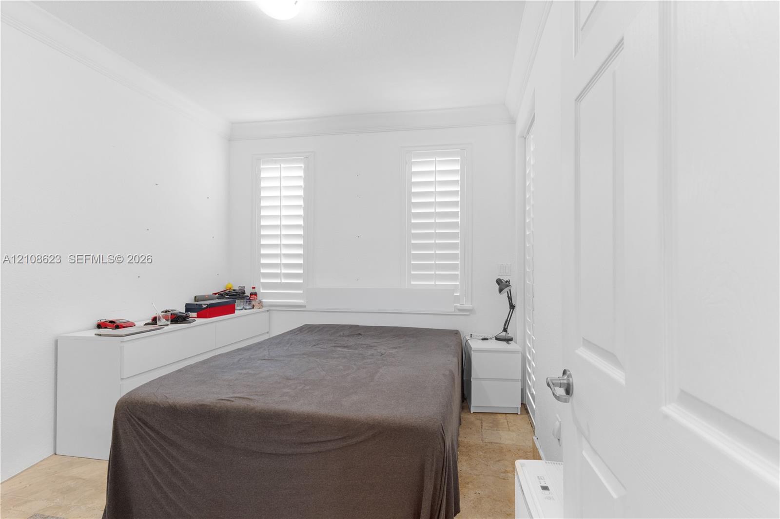 Room featuring white plantation shutters, crown molding, and stone-finish flooring