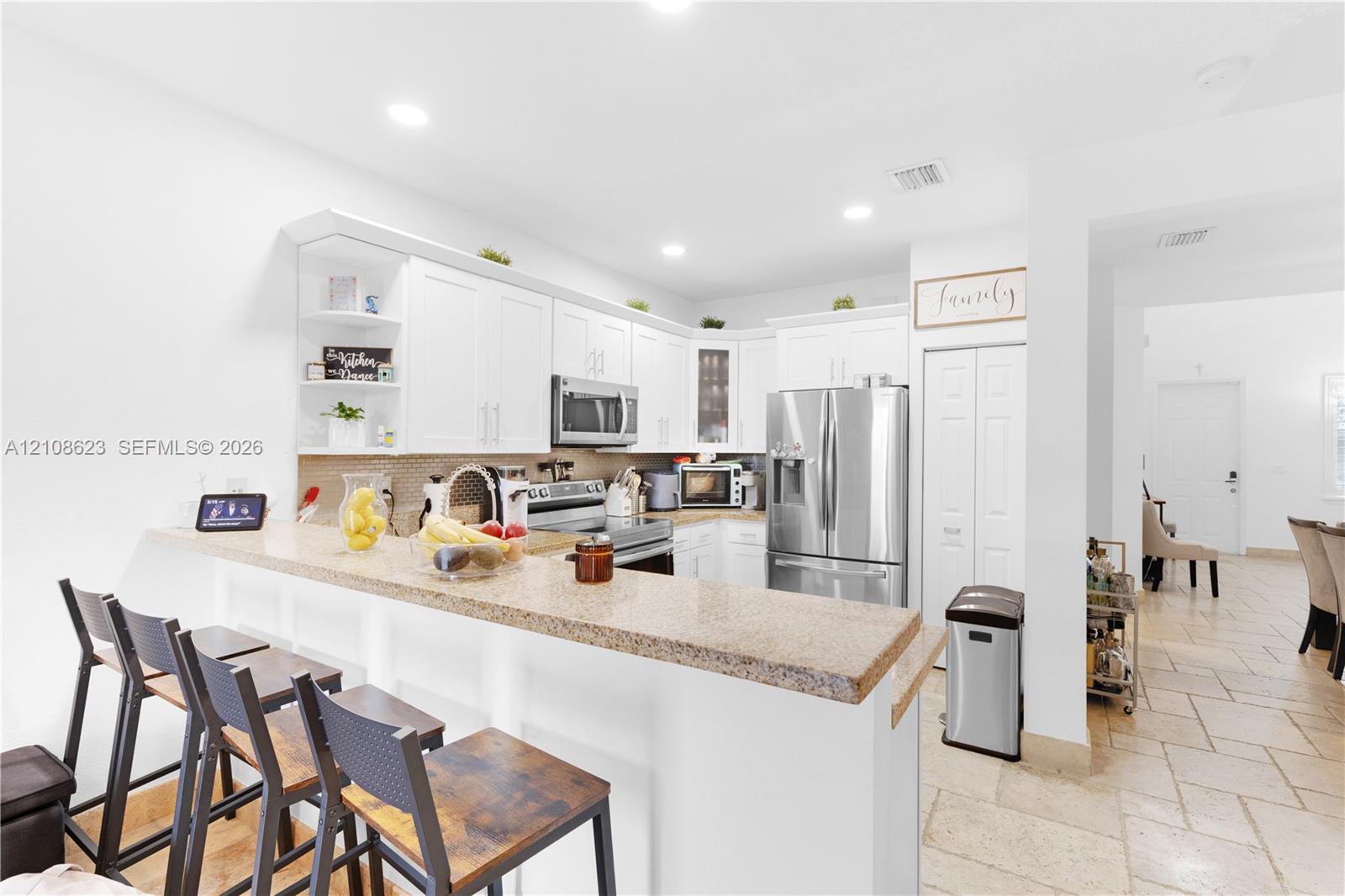 Kitchen featuring white cabinetry, stone-finish countertops, stainless steel appliances, a breakfast bar, and tile flooring
