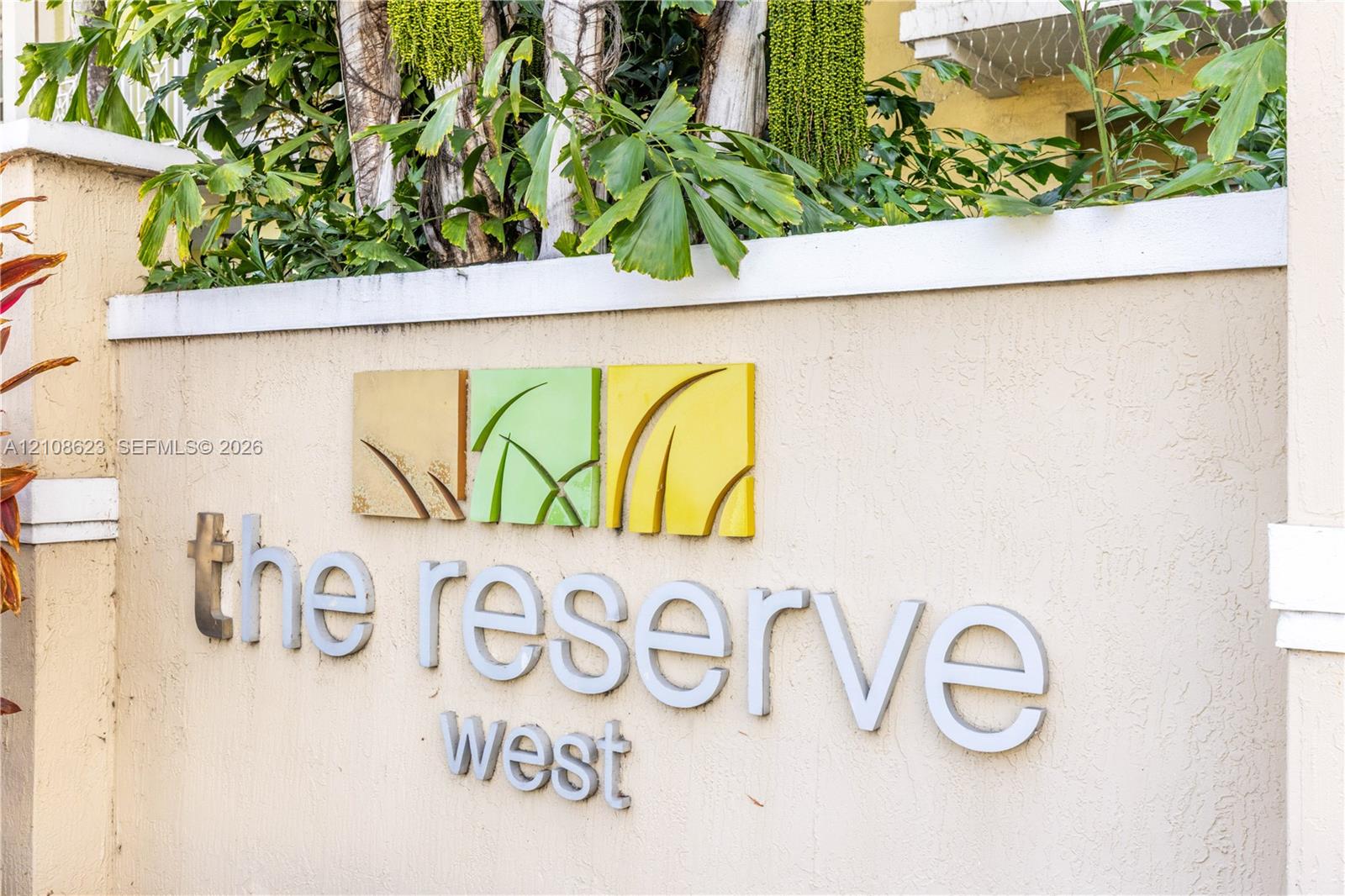 Stucco-finished masonry signage featuring dimensional lettering and sculptural metal detailing, complemented by mature tropical landscaping