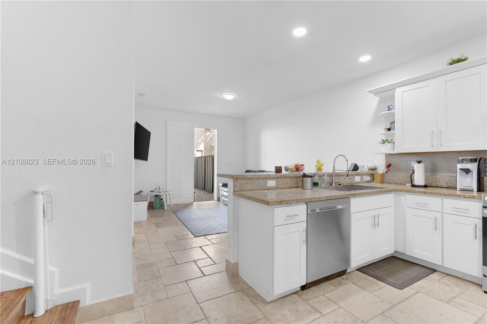 Kitchen featuring white shaker-style cabinetry, stone-finish countertops, stainless steel dishwasher, undermount sink, and stone-tile flooring