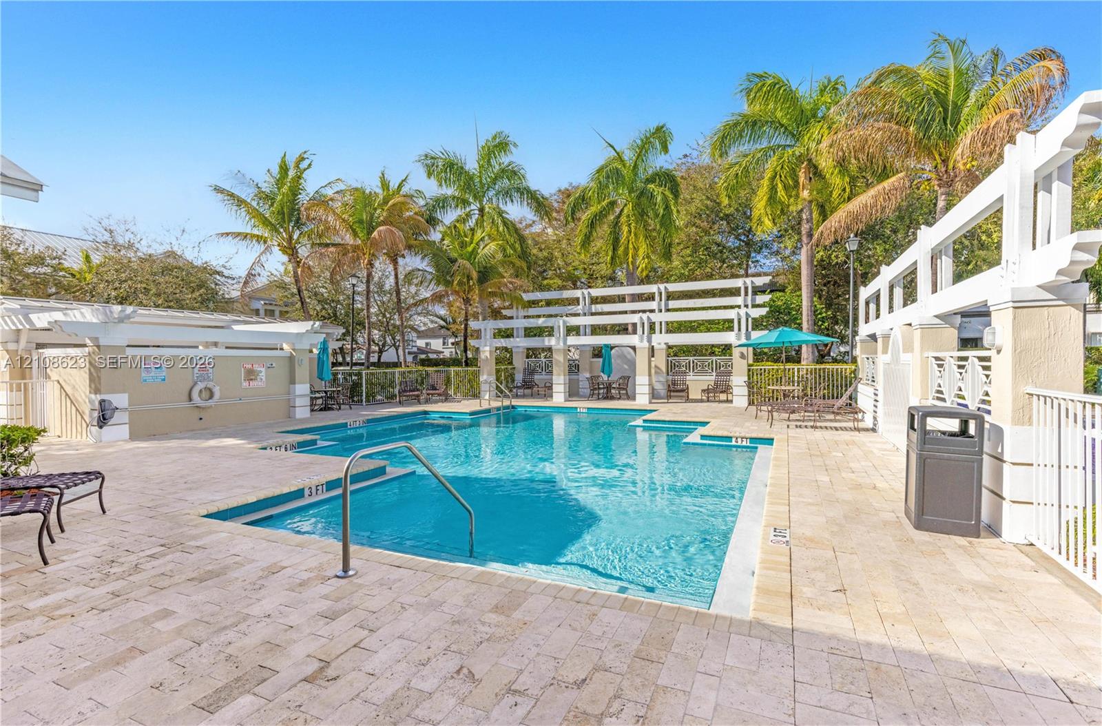 Swimming pool with paved surround, white trellis structures, and mature palm trees