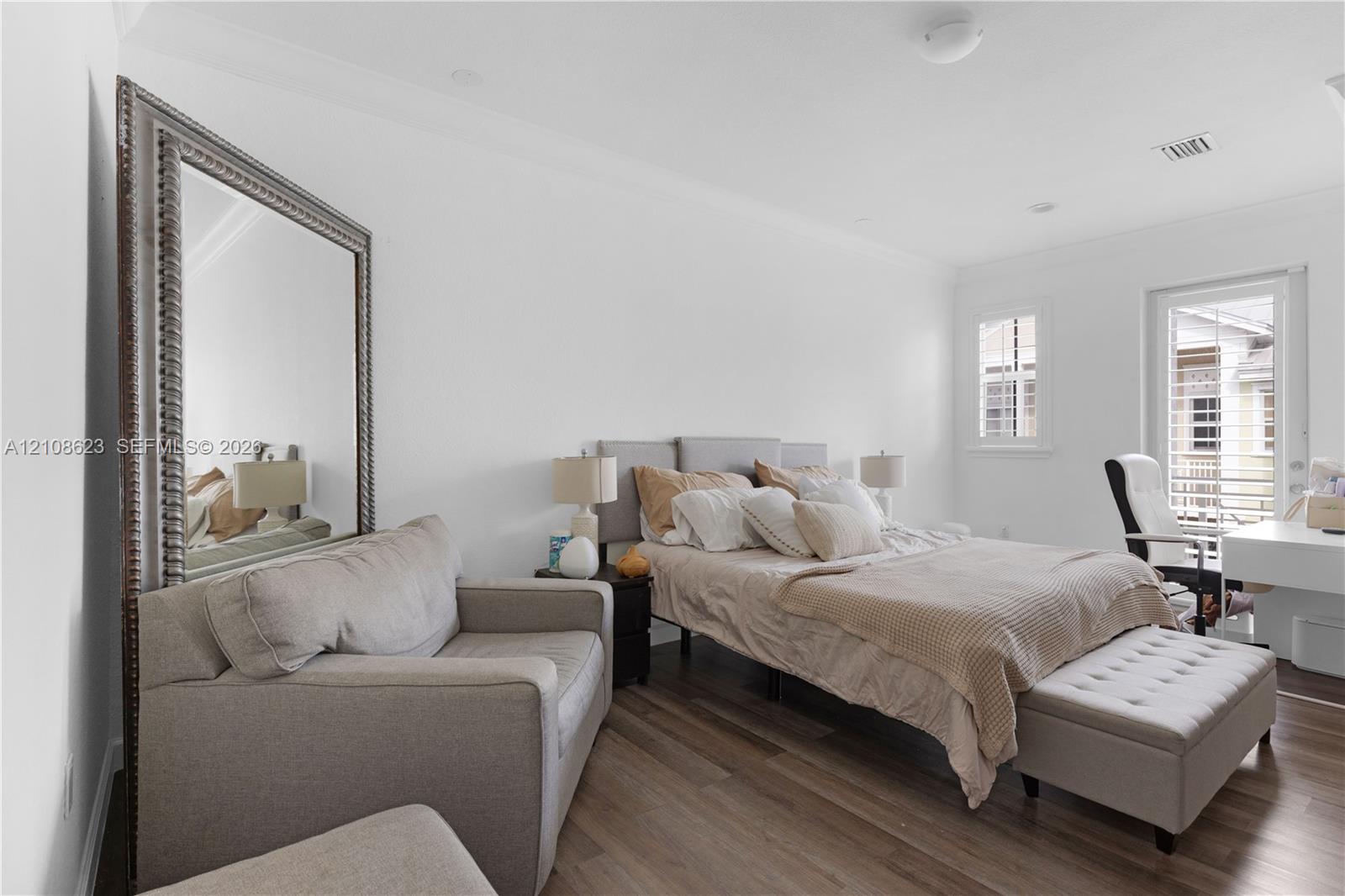 Neutral-toned room featuring wood-finish flooring, crown molding, and a full-length wall mirror with a metallic frame