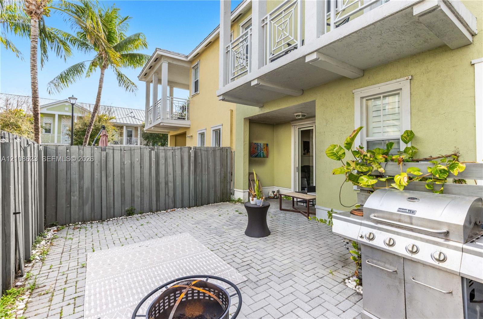 Private courtyard featuring herringbone-patterned stone pavers, privacy fencing, and two elevated balconies with geometric metal railings