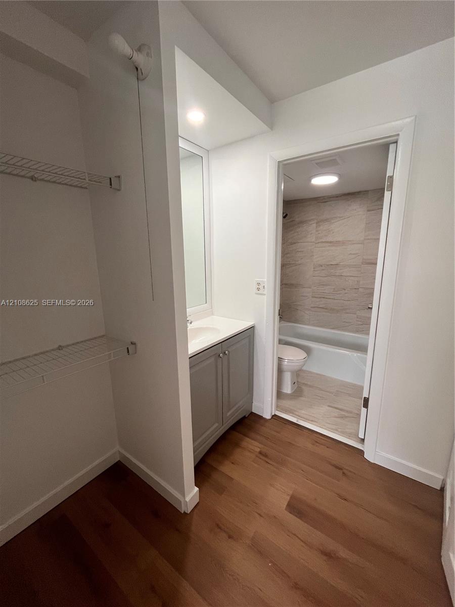 Bathroom featuring wood-finish flooring, a grey vanity with a solid-surface countertop, an inset sink, and a tiled shower-tub combination
