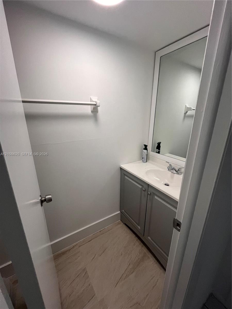 Bathroom featuring a vanity with grey cabinetry, a solid-surface countertop with an integrated basin, a wall-mounted mirror with a white frame, and wood-finish flooring