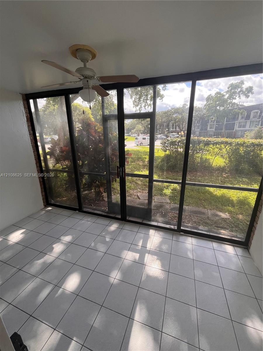 Enclosed sunroom featuring ceramic tile flooring, a ceiling fan with integrated lighting, and expansive floor-to-ceiling screen panels with sliding door access