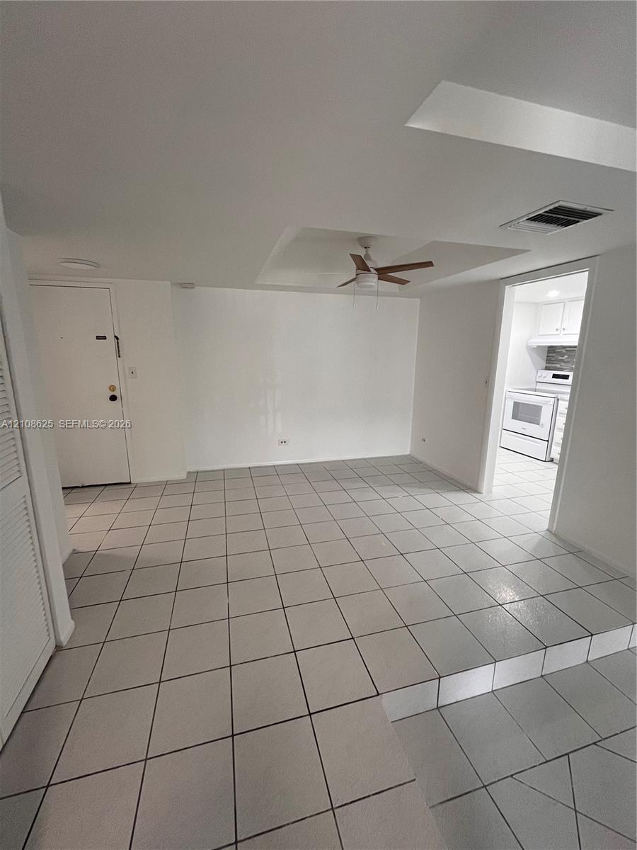 Interior space featuring a multi-level floor plan with ceramic tile flooring, a tray ceiling, and a central ceiling fan