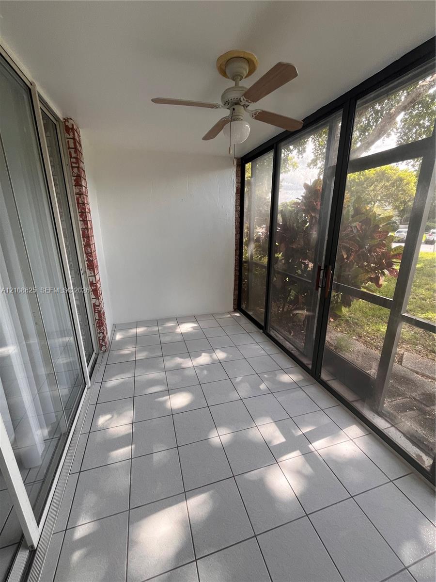 Enclosed patio featuring tile flooring, a ceiling fan with integrated light, floor-to-ceiling glass sliding doors, and a screened perimeter wall
