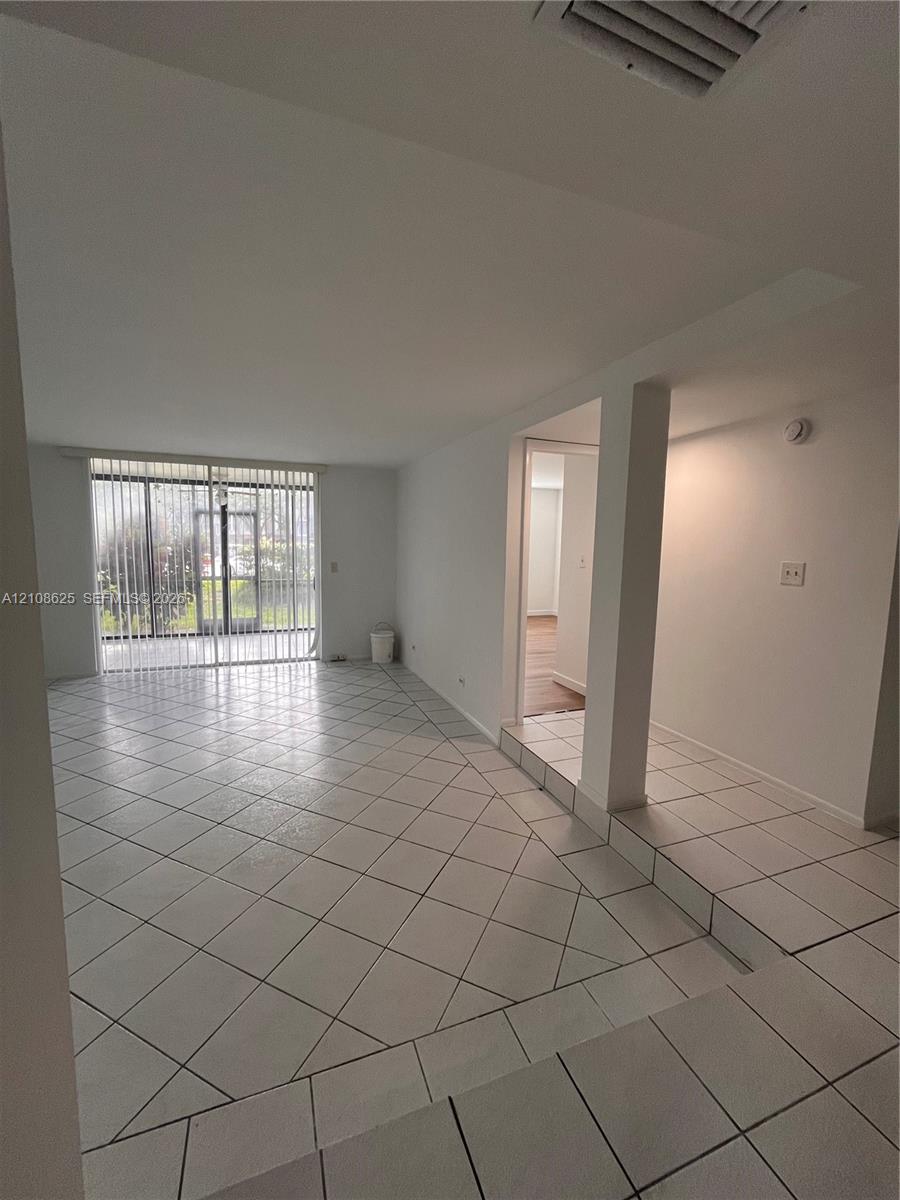 Open-concept interior featuring large-format ceramic tile flooring laid on the diagonal, architectural support column, and full-height sliding glass doors with vertical blinds