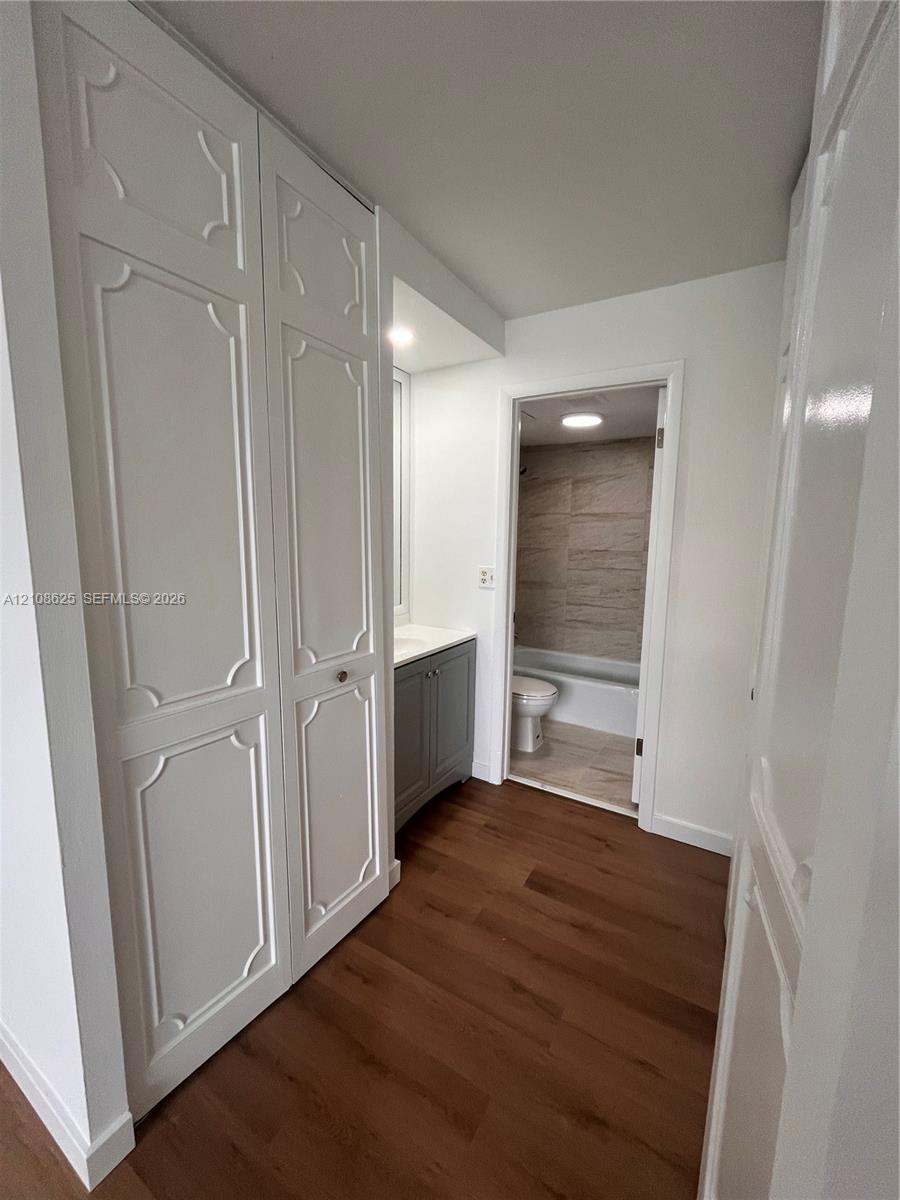 Wood-finish flooring, full-height cabinetry with decorative paneling, stone-topped vanity, and tile-surround bathtub