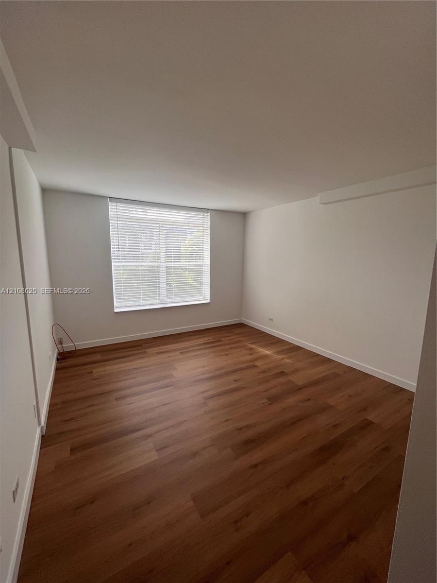 Interior room featuring wood-finish flooring, neutral walls, and a single window with installed horizontal blinds