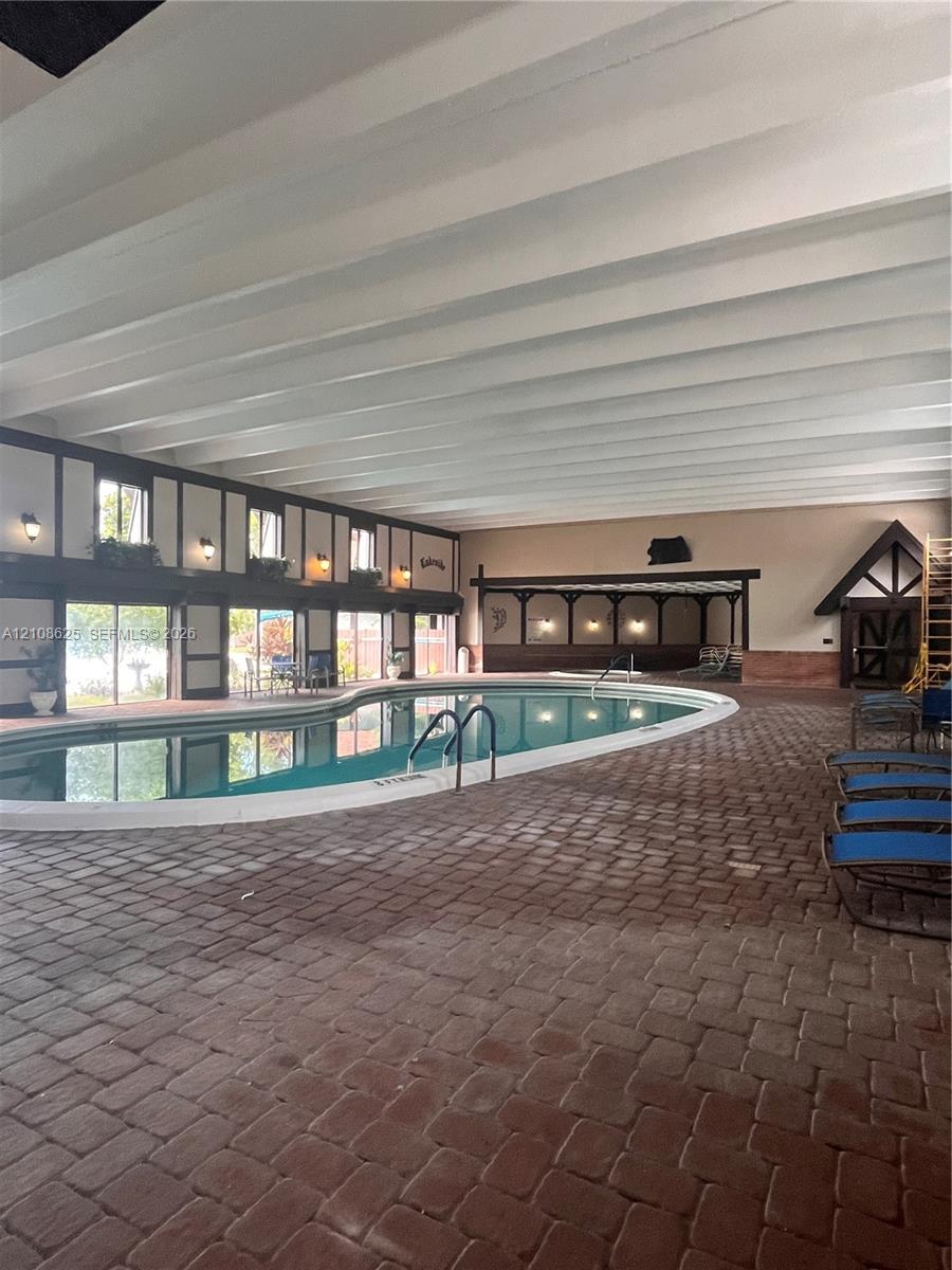 Indoor pool area featuring a brick paver floor, exposed beam ceiling, sliding glass doors, and half-timbered architectural detailing