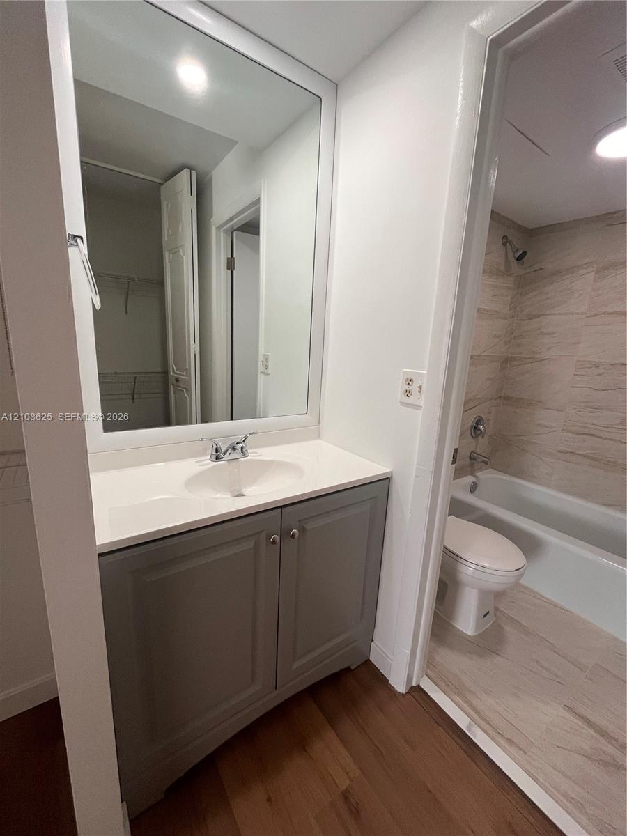 Bathroom featuring a grey vanity cabinet with a white countertop, large framed wall mirror, and a tile-surround bathtub