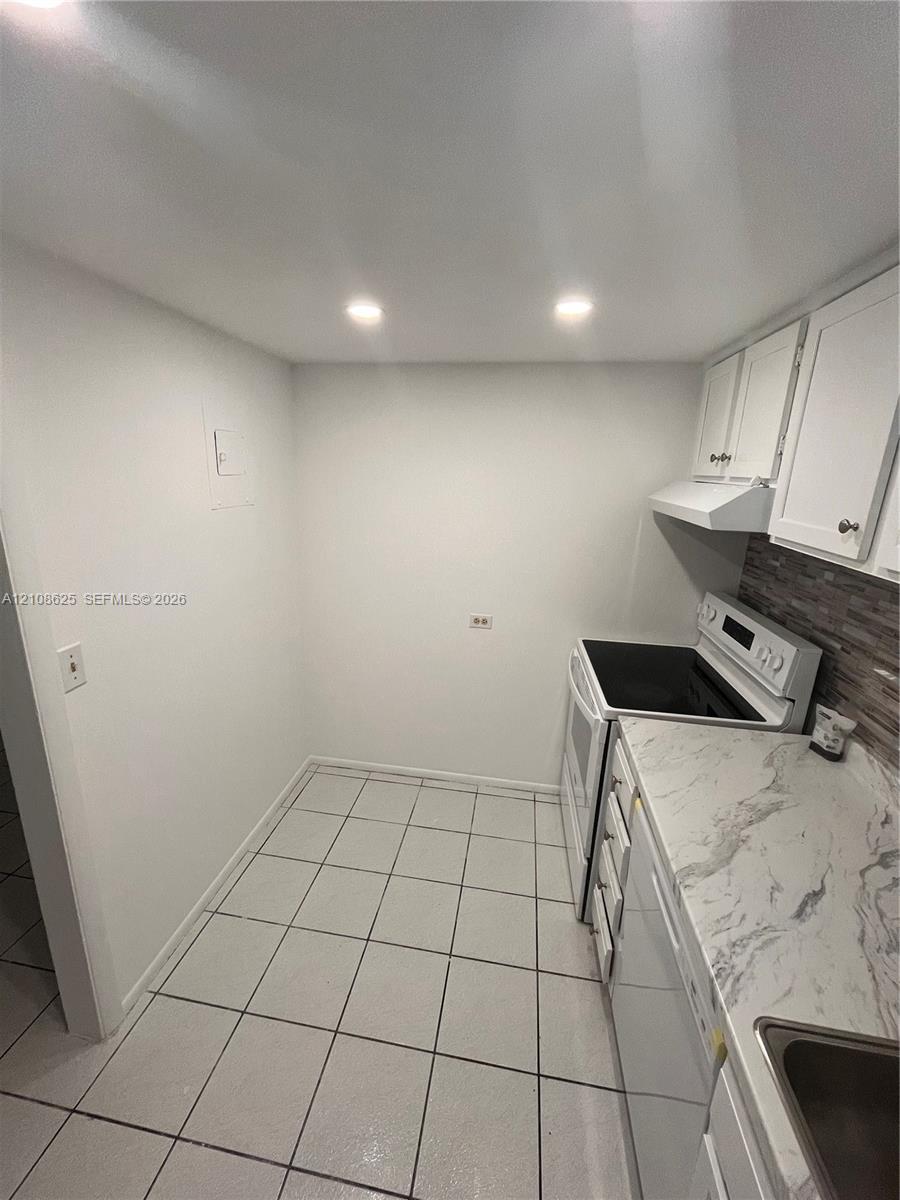 Kitchen featuring white cabinetry, stone-patterned countertops, recessed lighting, tile flooring, and a decorative backsplash