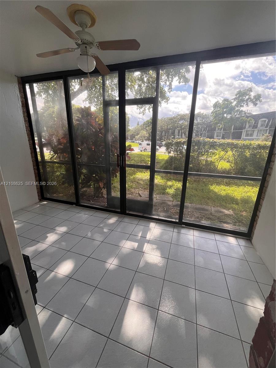 Enclosed patio featuring white tile flooring, expansive floor-to-ceiling screens, and a ceiling-mounted fan
