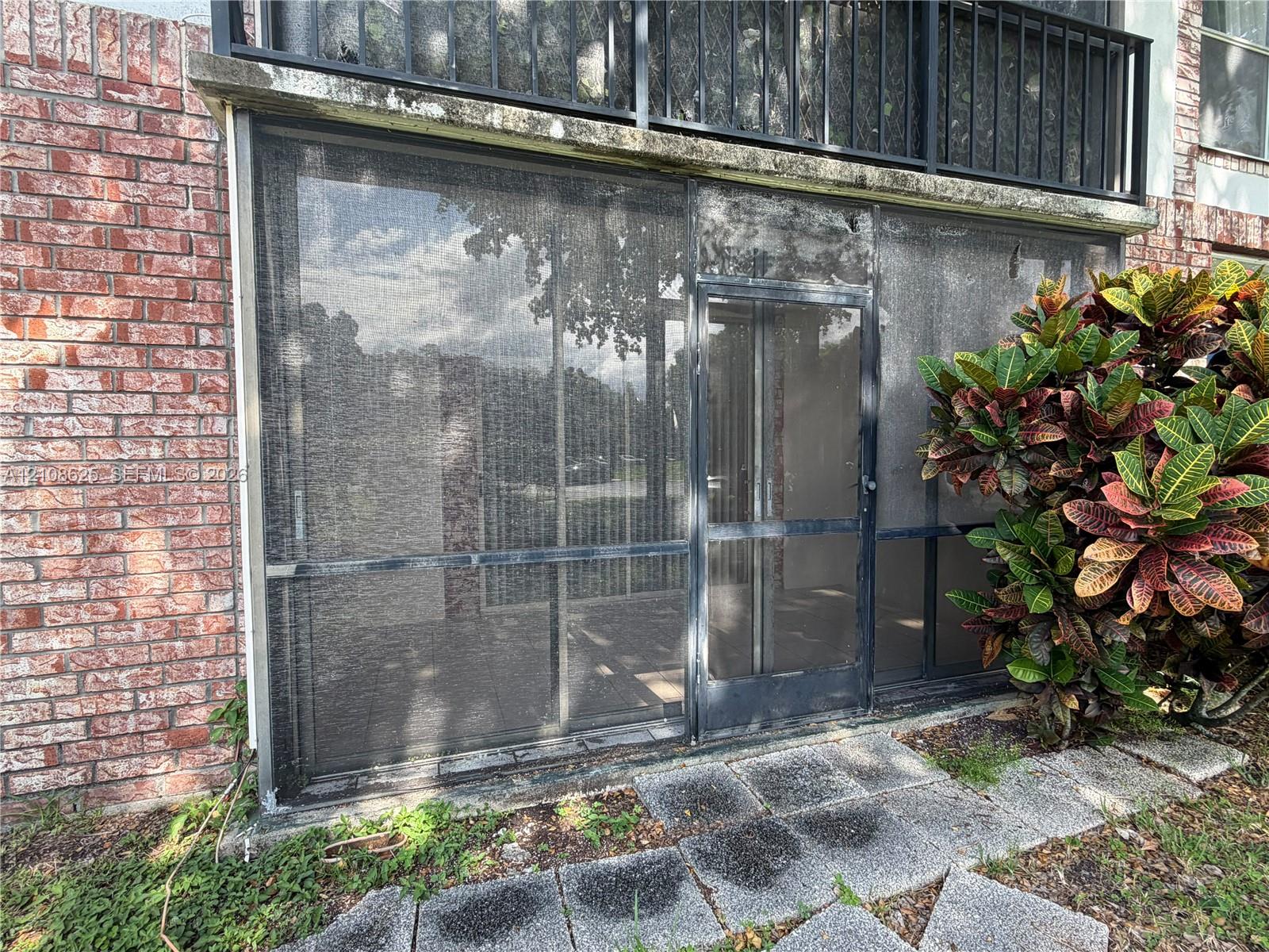 Screened-in enclosure featuring a red brick exterior, stone paver pathway, and black metal balcony railing