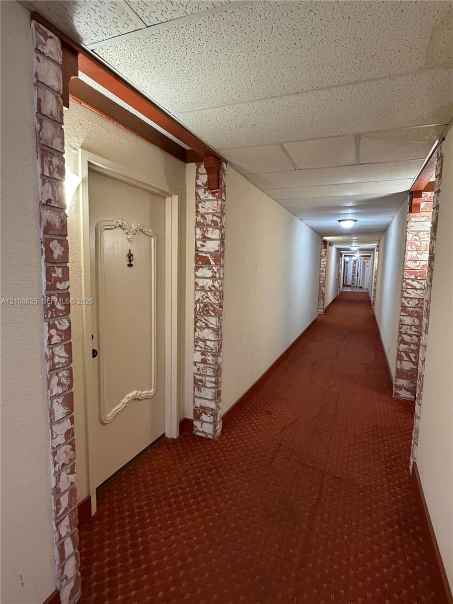 Hallway featuring decorative brick-clad columns, wood-beam accents, and recessed lighting
