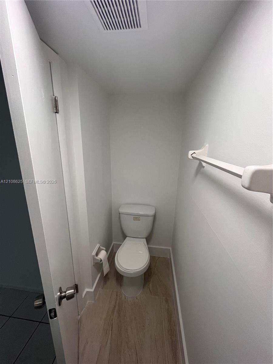 White porcelain commode, wood-finish flooring, and wall-mounted towel bar