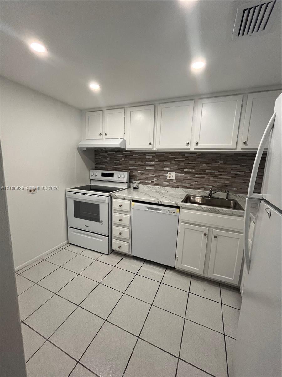 Kitchen featuring white cabinetry, stone-patterned countertops, a multi-tone tile backsplash, built-in appliances, and tile flooring