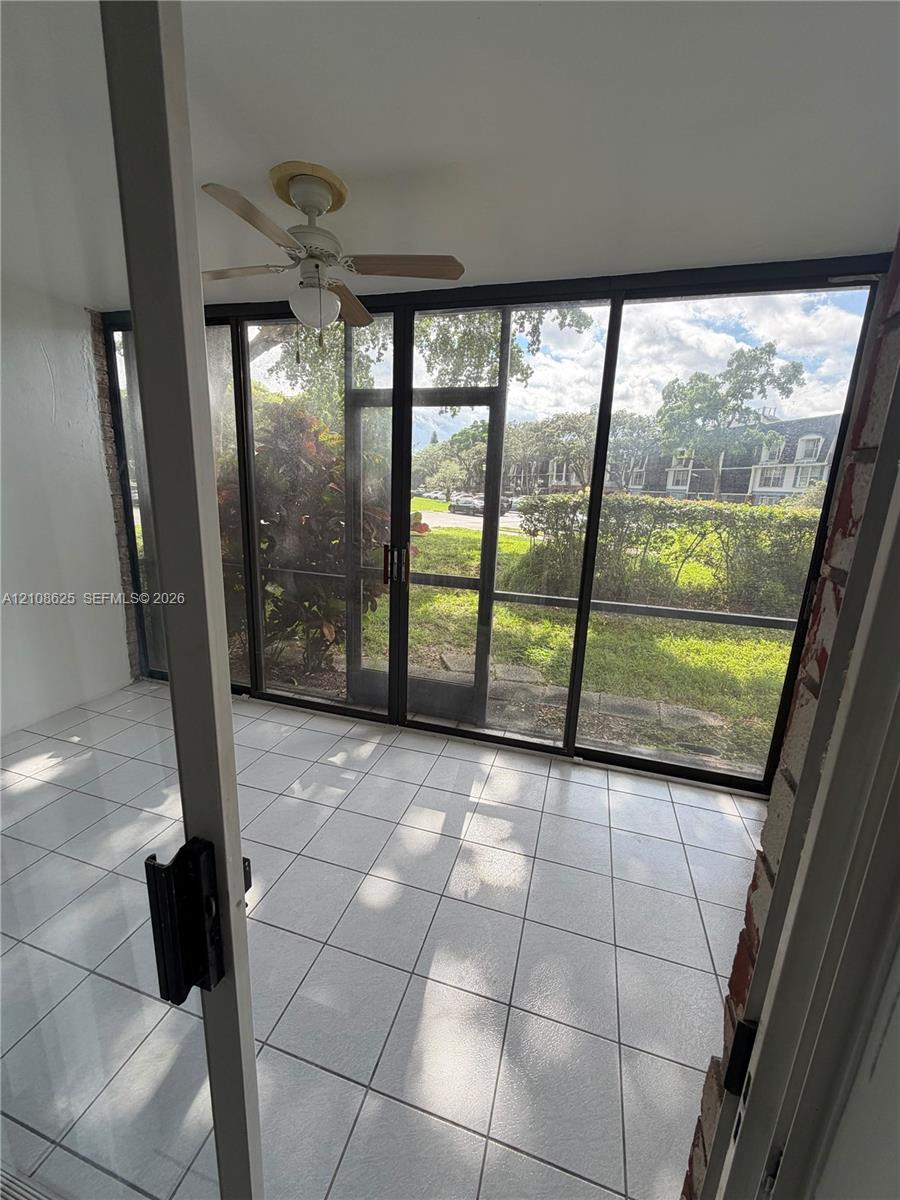 Enclosed patio featuring white tile flooring, ceiling fan with integrated lighting, and expansive screened panels