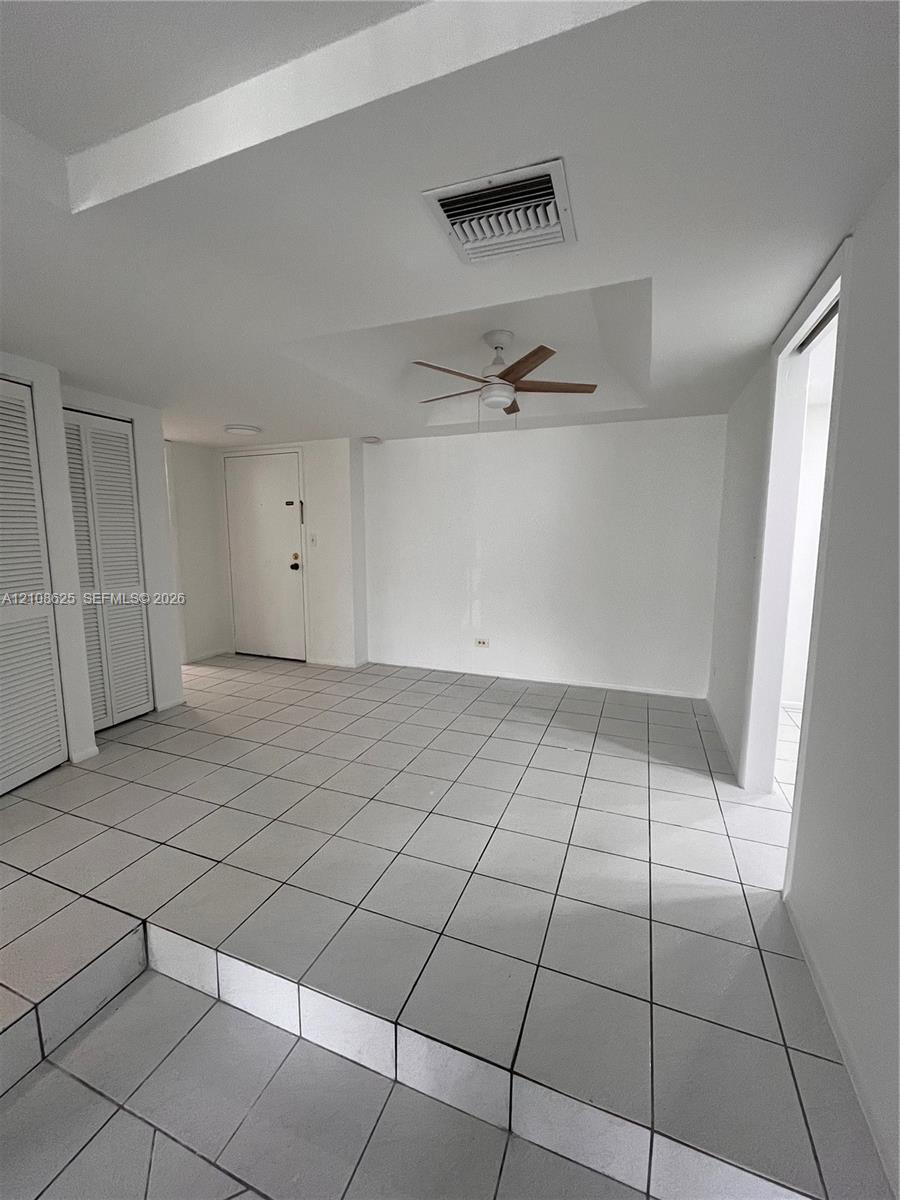 Interior space featuring large-format ceramic tile flooring, a tray ceiling, a ceiling fan, and dual louvered closet doors