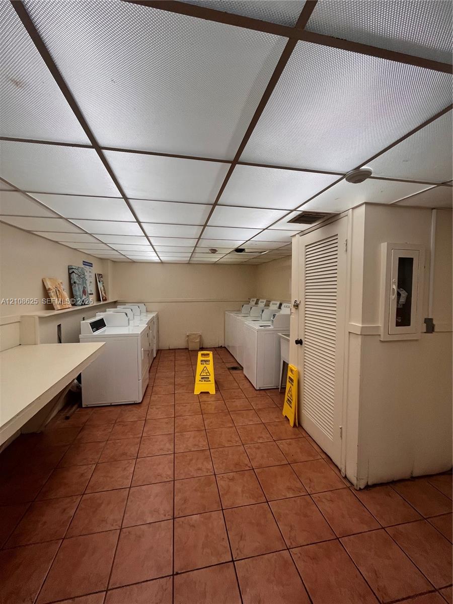 Laundry facility featuring ceramic tile flooring, a suspended grid ceiling, built-in folding counter, and multiple washing and drying units