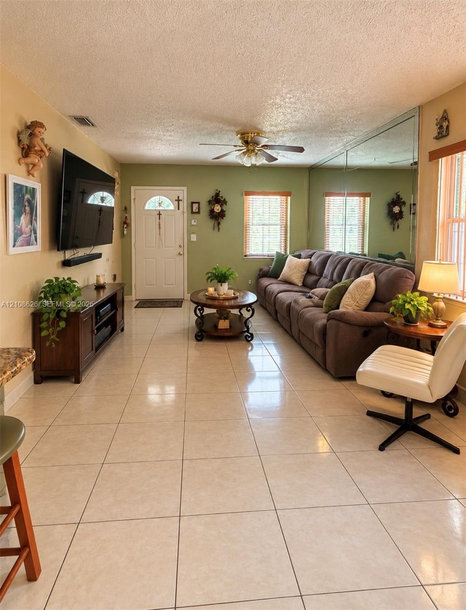 Ceramic tile flooring, mirrored wall accent, ceiling fan, and multiple windows with wood-finish blinds