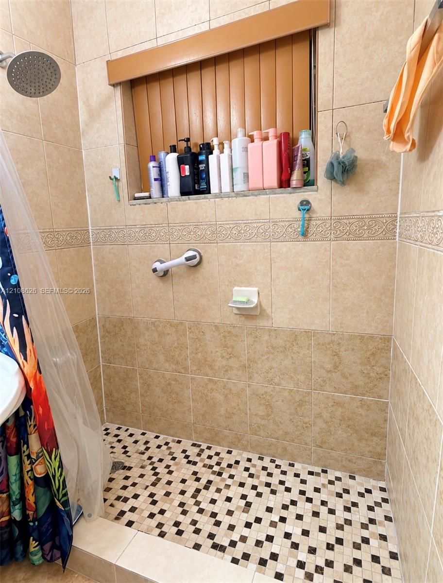 Walk-in shower enclosure featuring floor-to-ceiling tile, a decorative tile border, a built-in recessed shelf, and a mosaic-tile shower floor