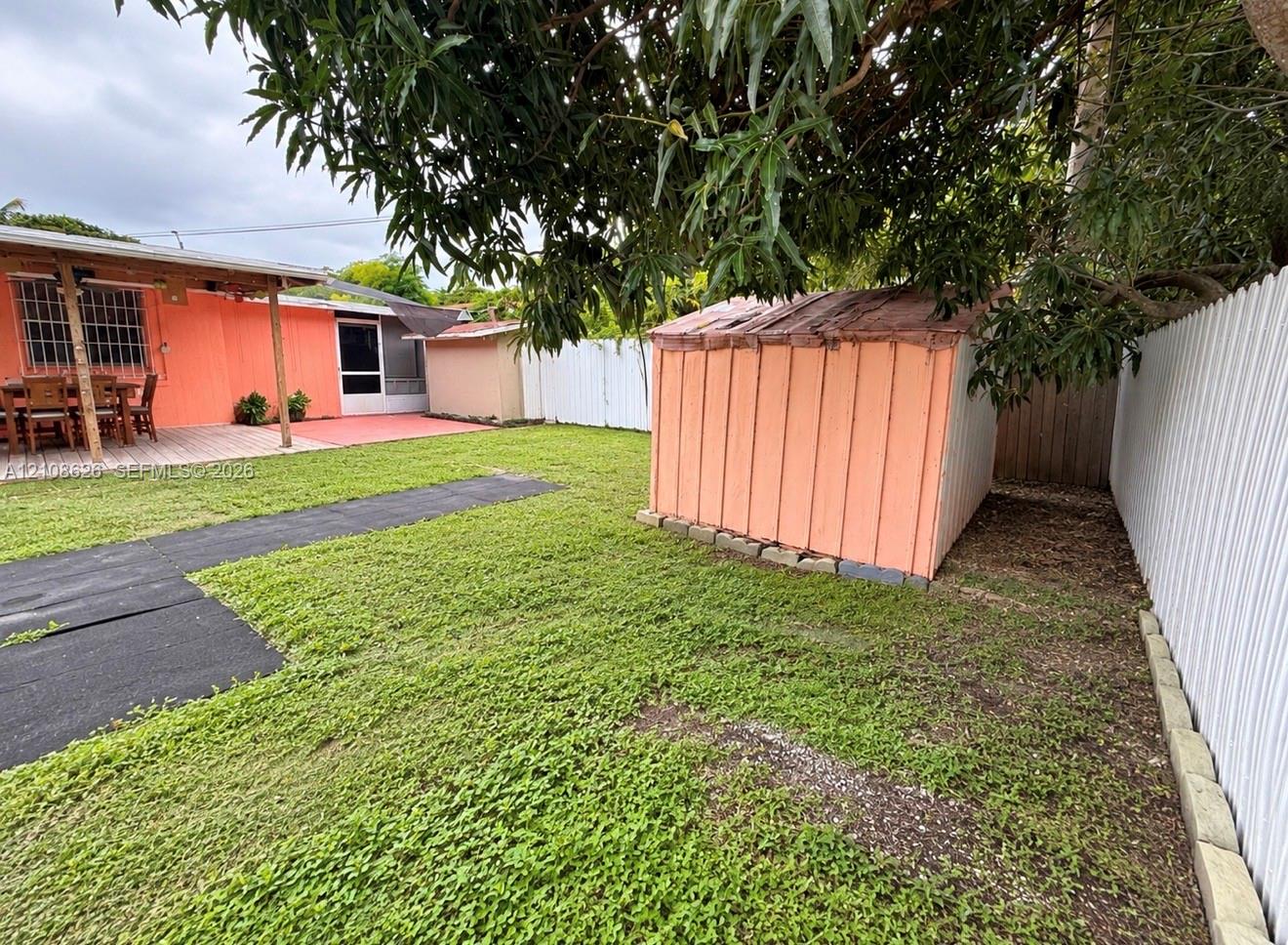 Backyard featuring a grass lawn, a detached storage structure, a paved patio, and perimeter fencing