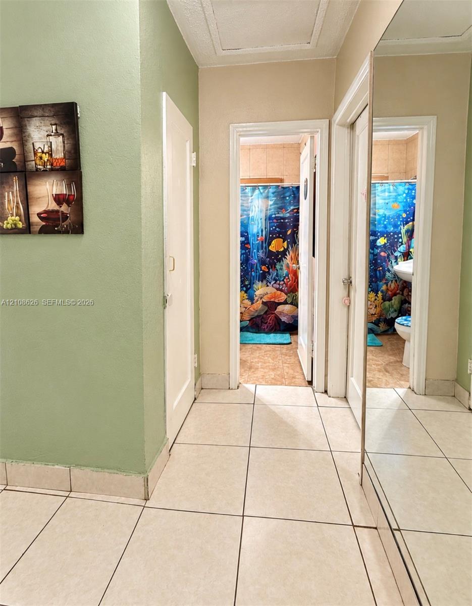 Hallway featuring large-format ceramic tile flooring, full-length wall mirror, and solid-core interior doors