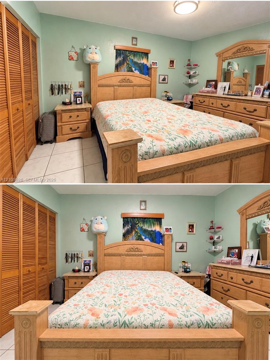 Bedroom featuring floor-to-ceiling louvered-door closets, tile flooring, and a glass-paneled wall-mounted corner shelf