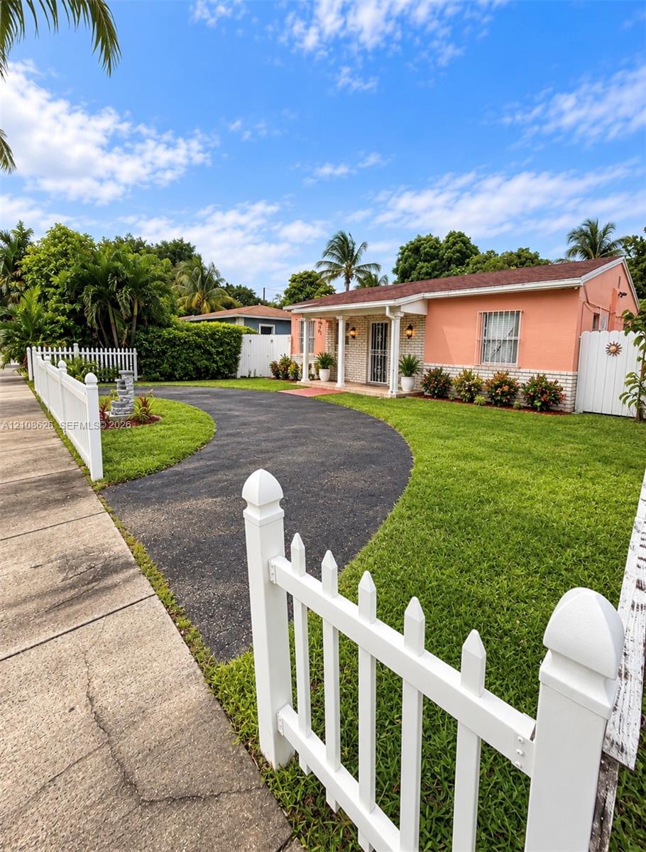 Single-story exterior featuring stucco and brick facade, a curved asphalt driveway, and perimeter white picket fencing
