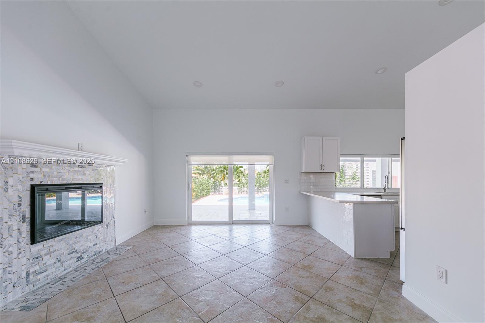 Open-concept space featuring tile flooring, stone-surround fireplace with a mantel, recessed lighting, and a breakfast bar with stone-finish countertops