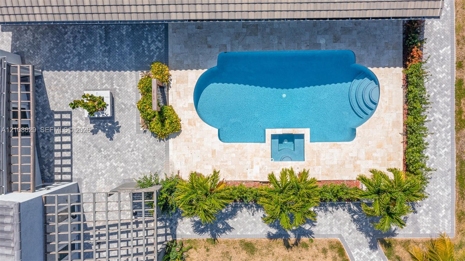 Aerial perspective of an outdoor space featuring a custom-shaped swimming pool with an integrated spa, stone paver decking, and a wooden pergola structure