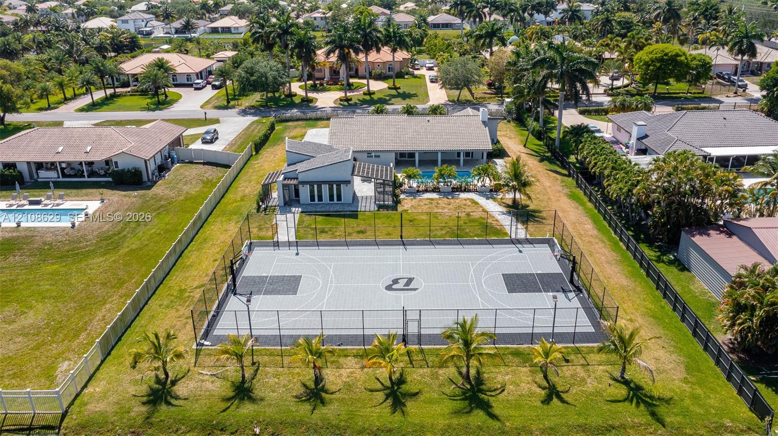 Private fenced basketball court with modular surfacing, expansive rear grounds, mature palm trees, and swimming pool
