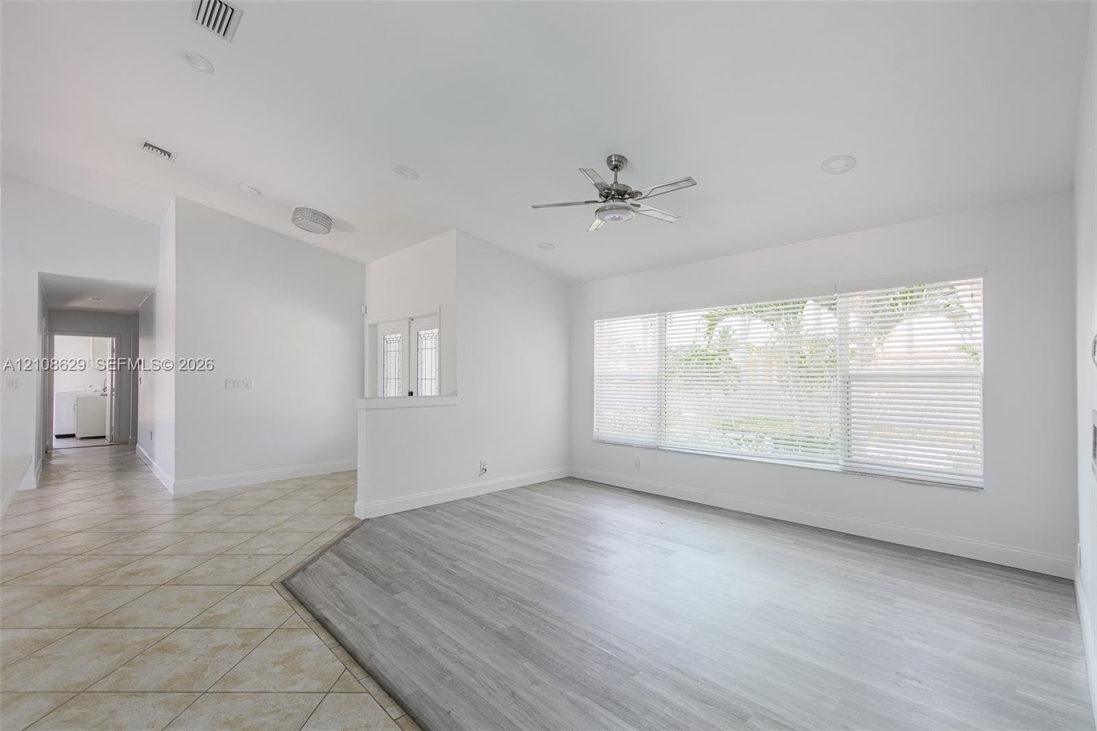 Open-concept interior featuring light gray wood-finish flooring, ceramic tile flooring, a multi-blade ceiling fan, and large windows with horizontal blinds